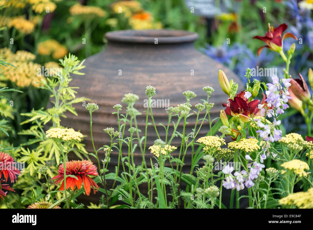 Wild flowers mixed, yellow, orange, crimson and blue around a copper colored urn. Stock Photo