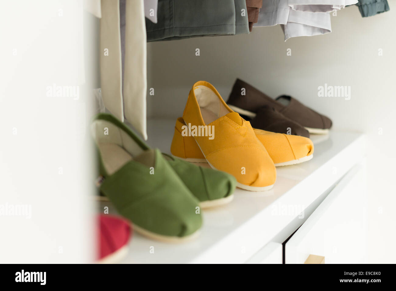 Row of new casual clothing on hangers at shop with four colorful pairs of shoes under it. Clothes presented as in wardrobe. Stock Photo