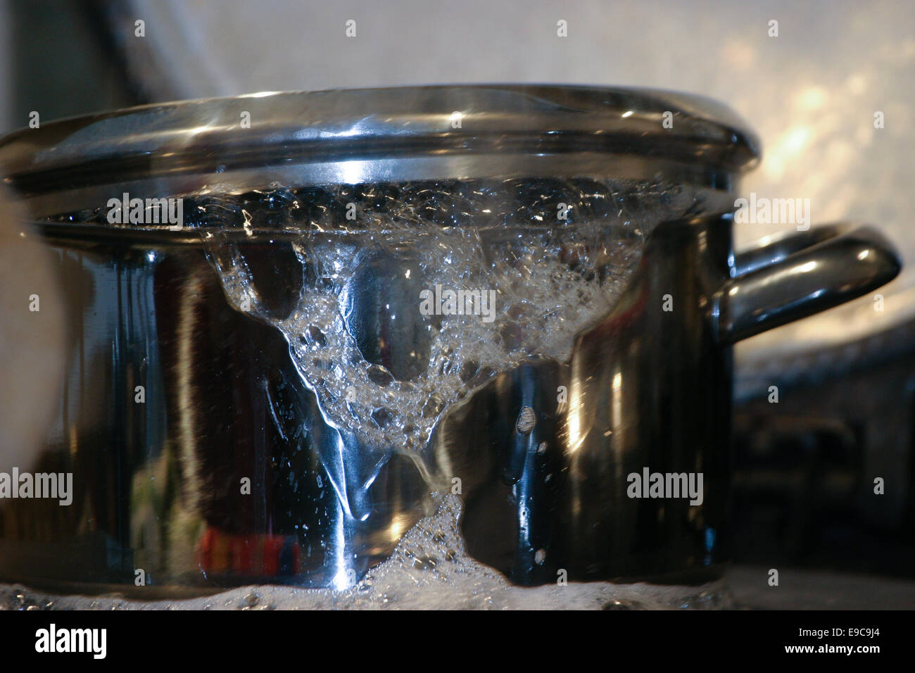 Water boiling over from a saucepan with lid.  Froth on the side of the pan. Stock Photo