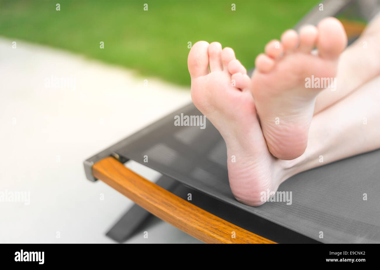 Focus on crossed feet of person lying and tanning on gray sunbed. Green