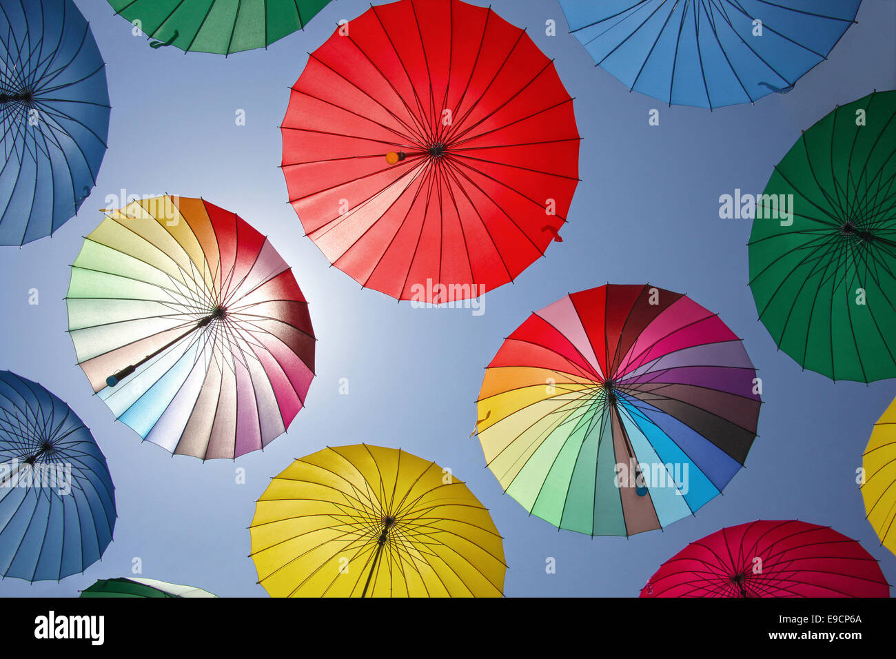 Collection of multi colored umbrellas hanging up in an open position over a street offering shade & protection from the elements Stock Photo