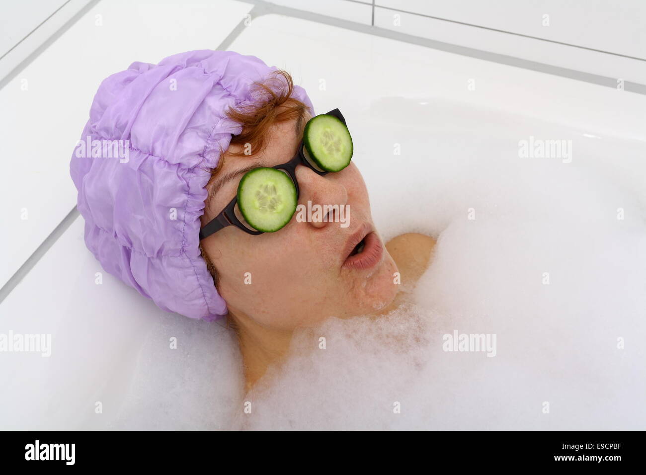 Mature woman in bathtub with cucumber slices on glasses, spa Stock Photo