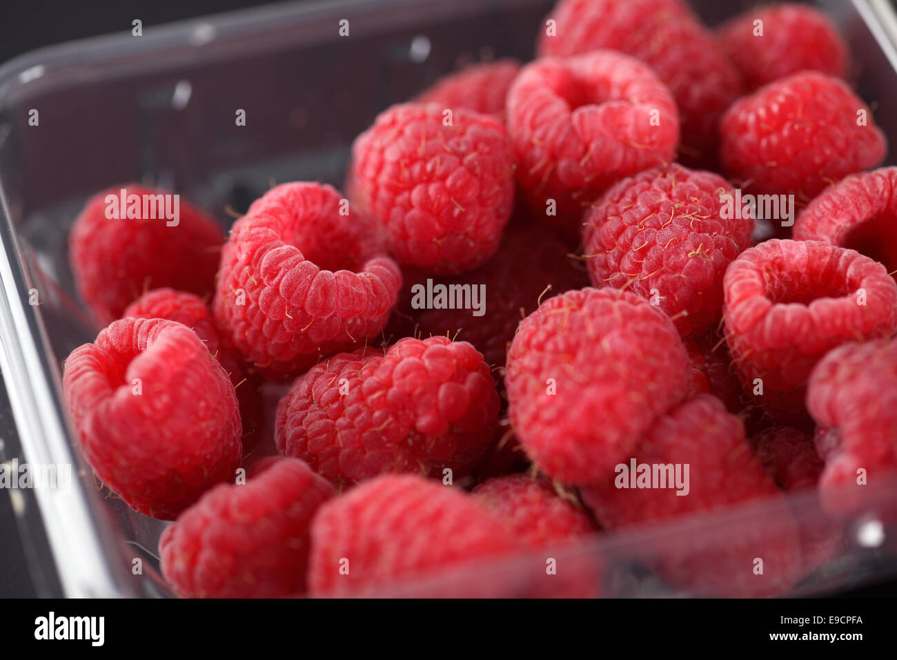 Fresh raspberries in plastic container on black background Stock Photo