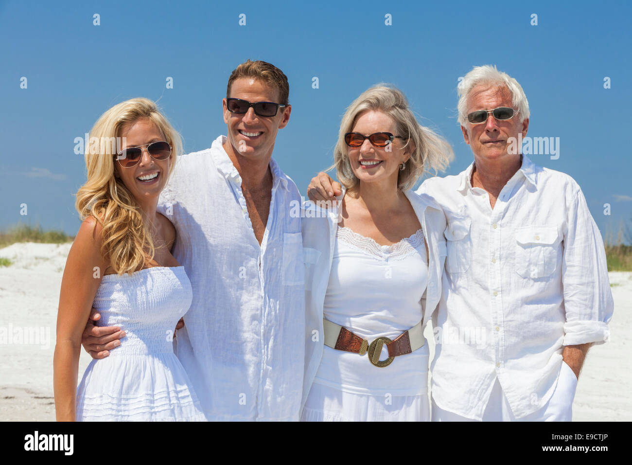 Four people, two seniors, couples or family generations, wearing white clothes together having fun on tropical beach vacation Stock Photo