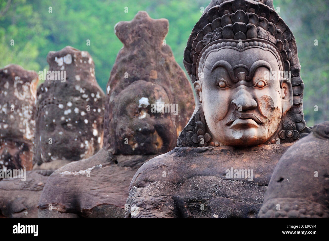 Stone figures line a causeway leading to  Angkor Thom, showing the demons (asuras) wearing military headdress  - Siem Reap, Cambodia, Southeast Asia Stock Photo