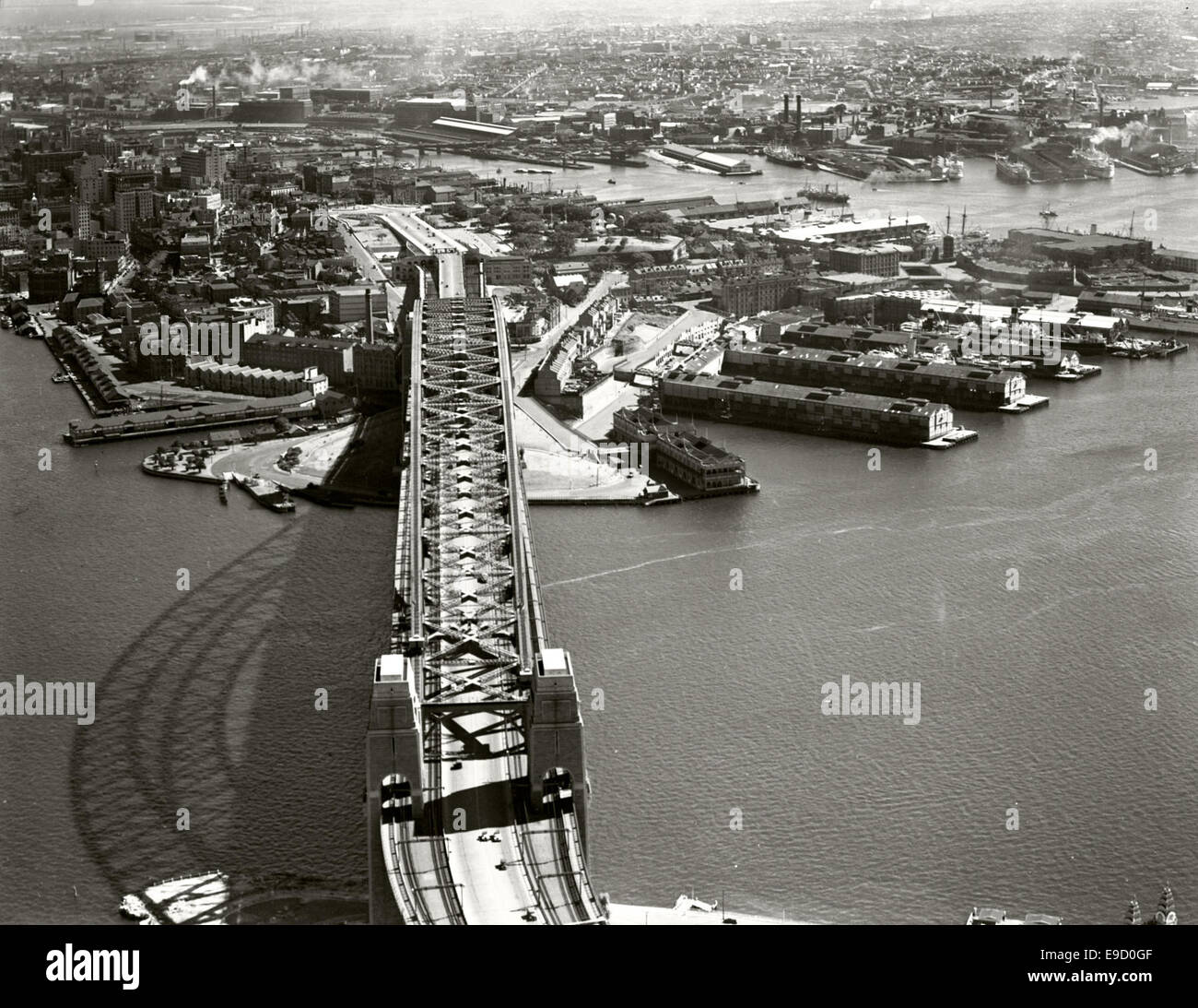 This aerial photograph captures a southern view of the Sydney Harbour Bridge, showcasing the city’s skyline and water features. The image is part of the Adastra Aerial Survey Collection, documenting Sydney’s landmarks from the sky. Stock Photo