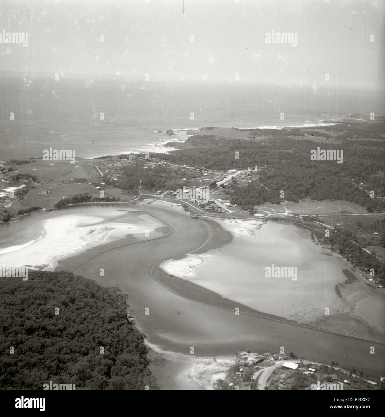 An aerial photograph of Narooma, New South Wales, looking southeast. The image shows the town's coastline and the surrounding landscape, captured as part of the Adastra Aerial Survey Collection. It highlights the beauty of the natural environment in this coastal area. Stock Photo
