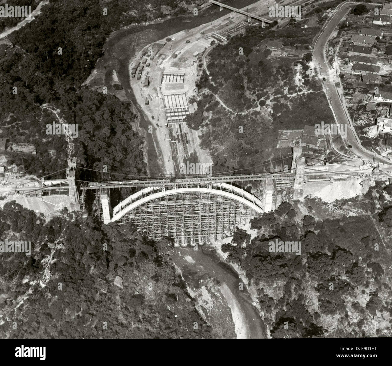 An aerial photograph of a suspension bridge under construction, captured as part of the Adastra Aerial Survey Collection. The image provides a detailed view of the bridge construction, with a focus on the engineering and design elements. Stock Photo