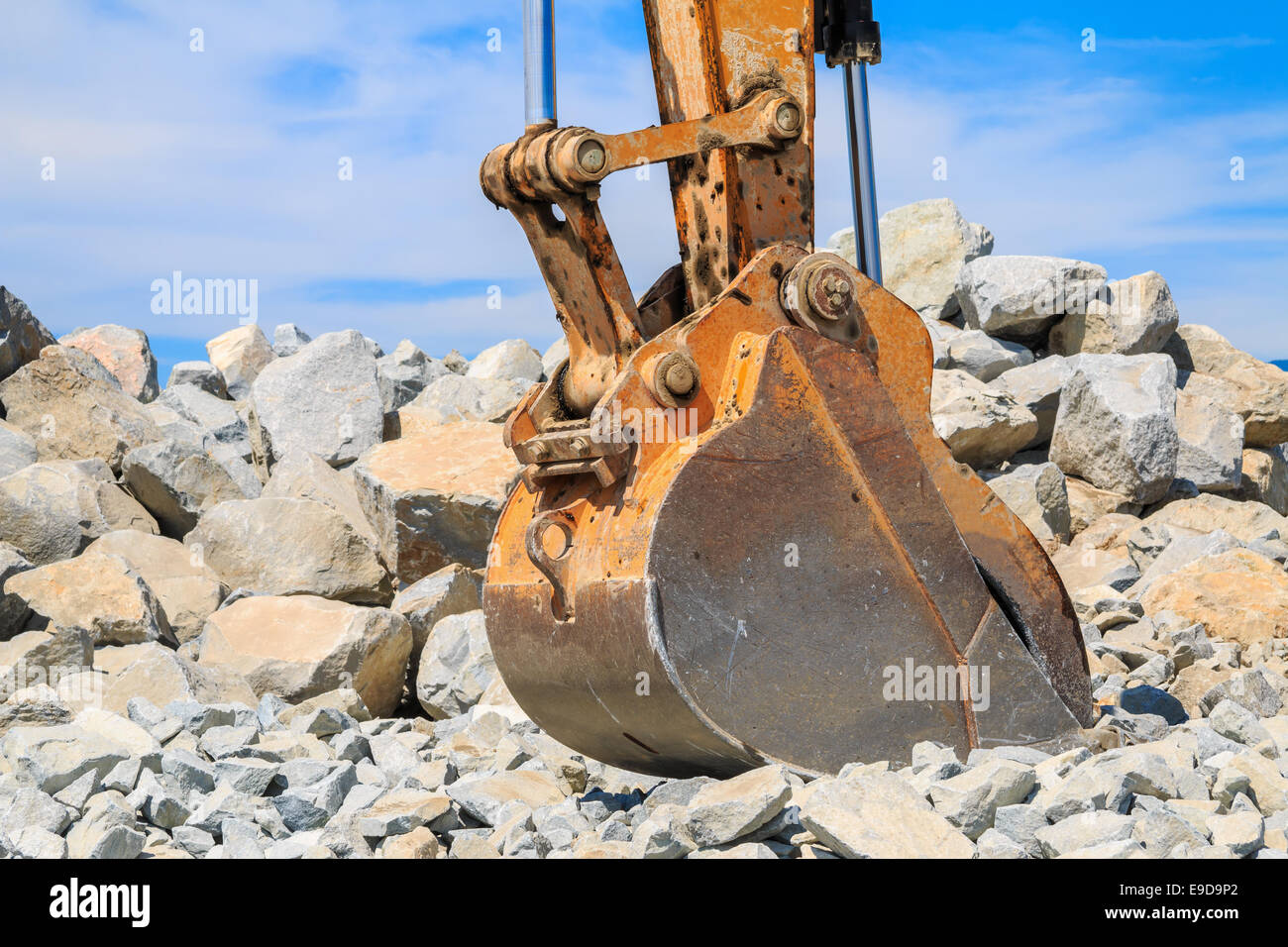 Backhoe bucket with a large pile of rocks in the background against a