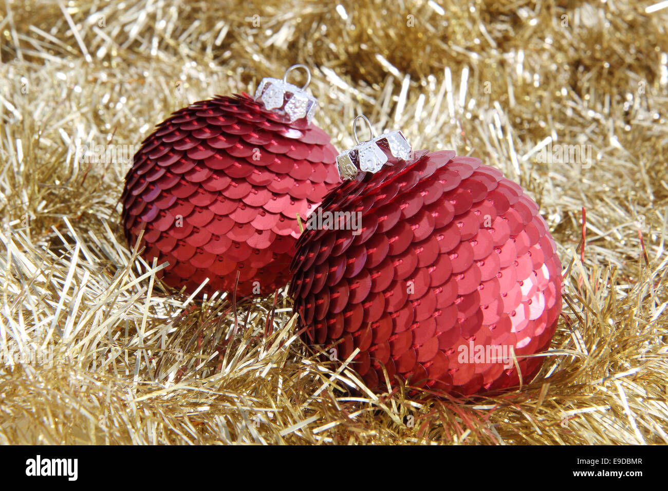 Two red Christmas sequin baubles on golden tinsel. Stock Photo