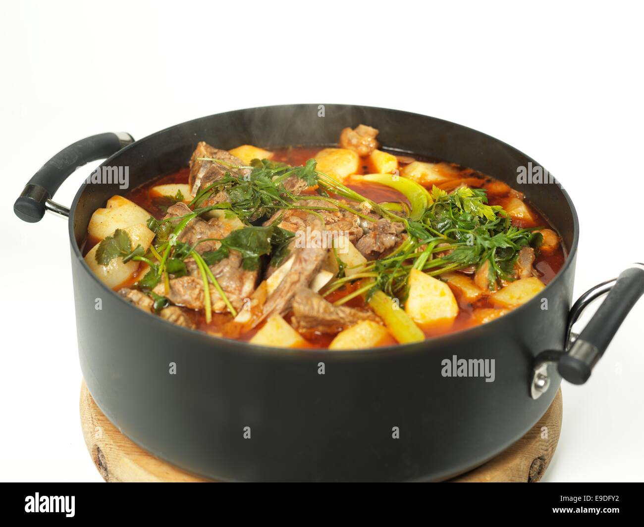 Tasty meat stew and herbs in black pot on the white background Stock Photo