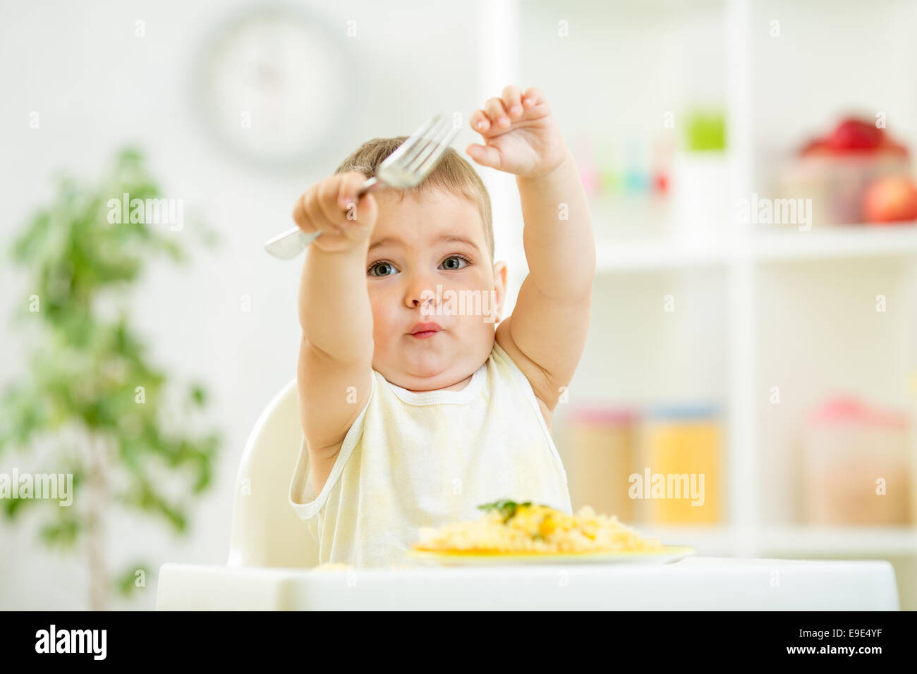 one year old kid boy in a highchair for feeding with a fork and Stock Photo