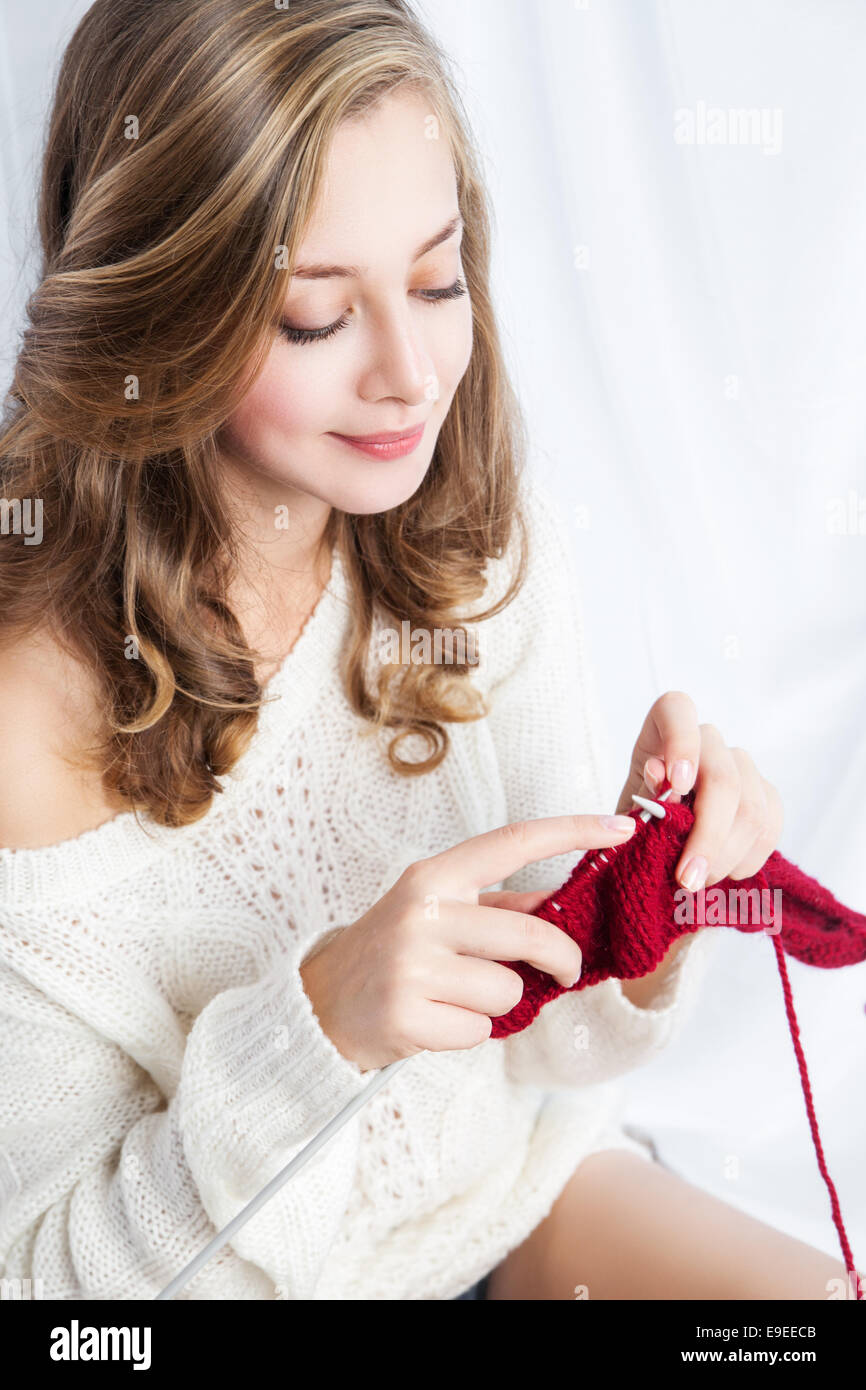 Portrait of charming girl in sweater sitting on windowsill and knitting