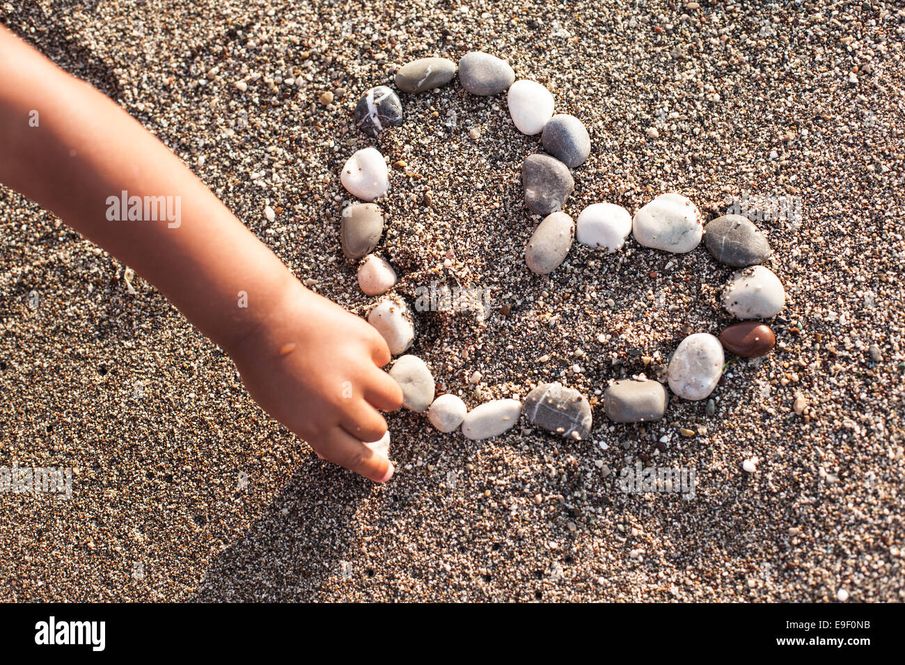 Baby's hand making heart of marine shingles on the sand. Stock Photo