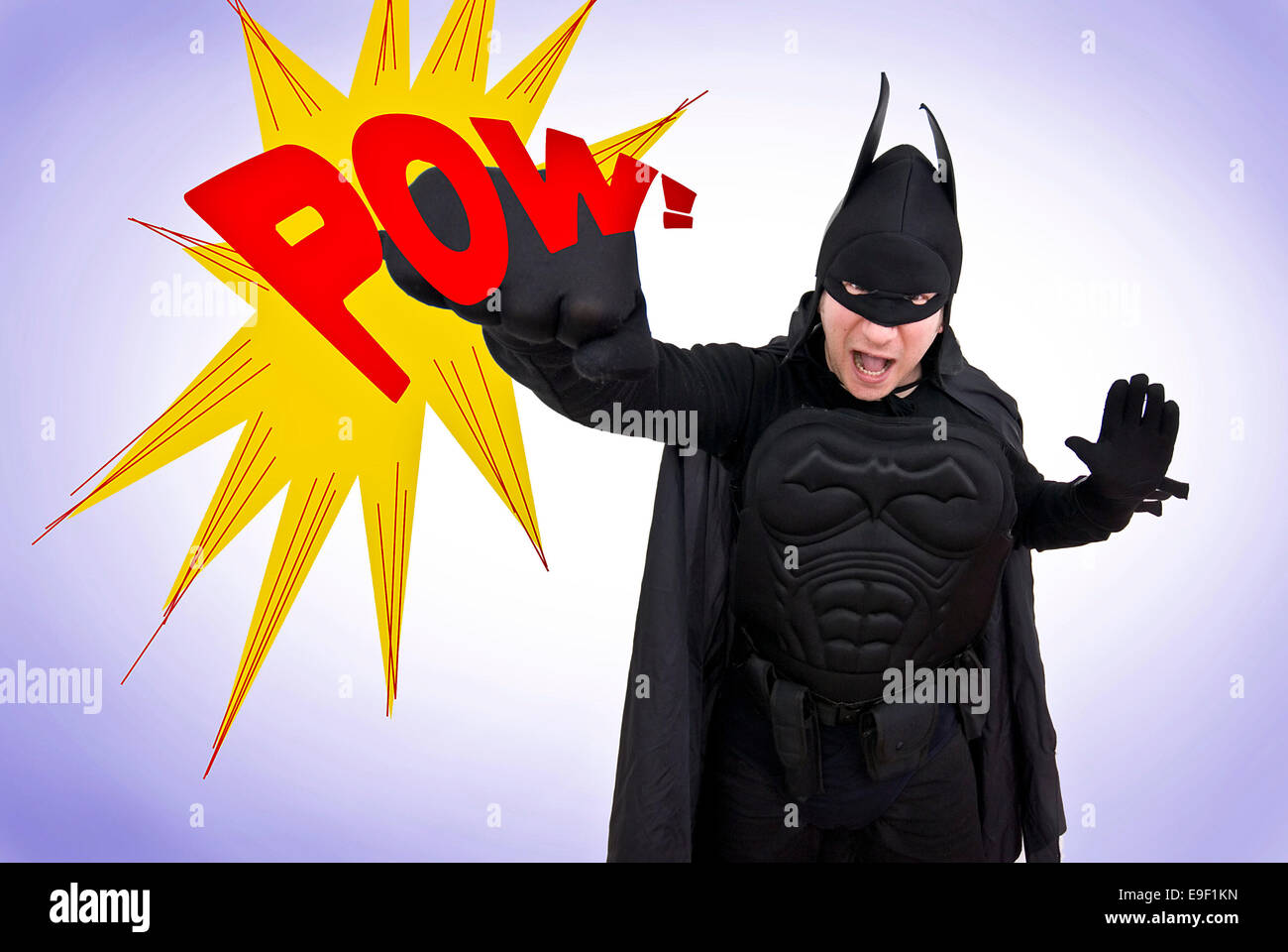 a man in a comedy batman costume punches the air with a giant POW sign, like the classic tv show Stock Photo