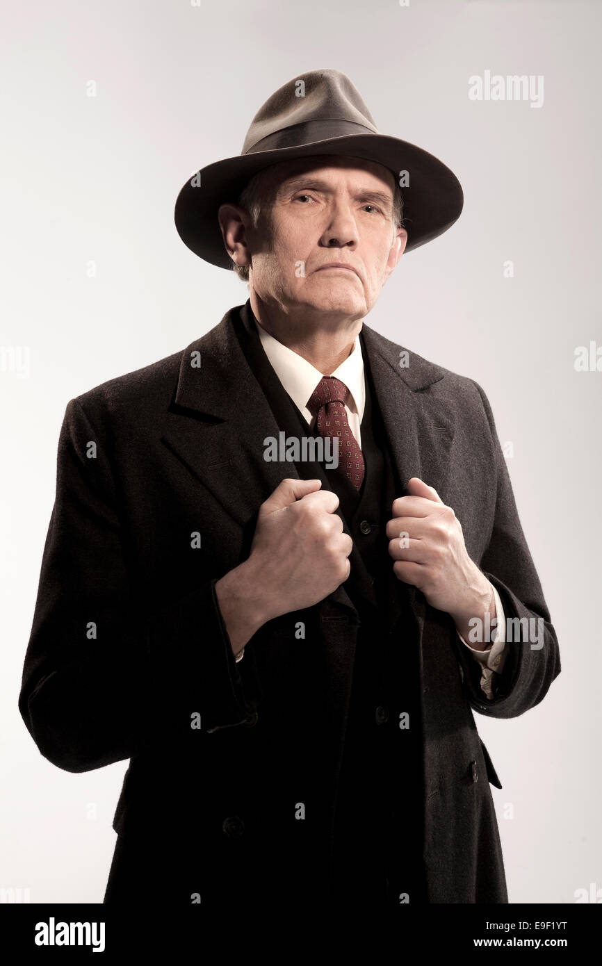 old characterful man in trilby hat and long coat looking like a detective / policeman / gangster in costume shot against white Stock Photo