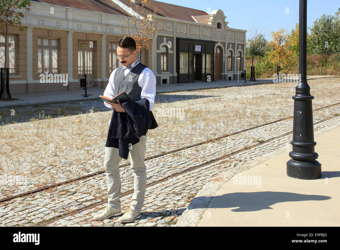 Man with mustache walking along the rails reading book wering vest in the old days of vintage city Stock Photo