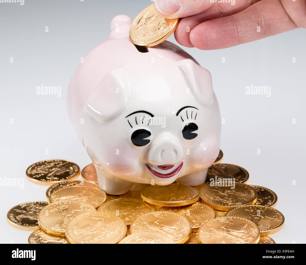 Hand placing gold coin into piggy bank Stock Photo