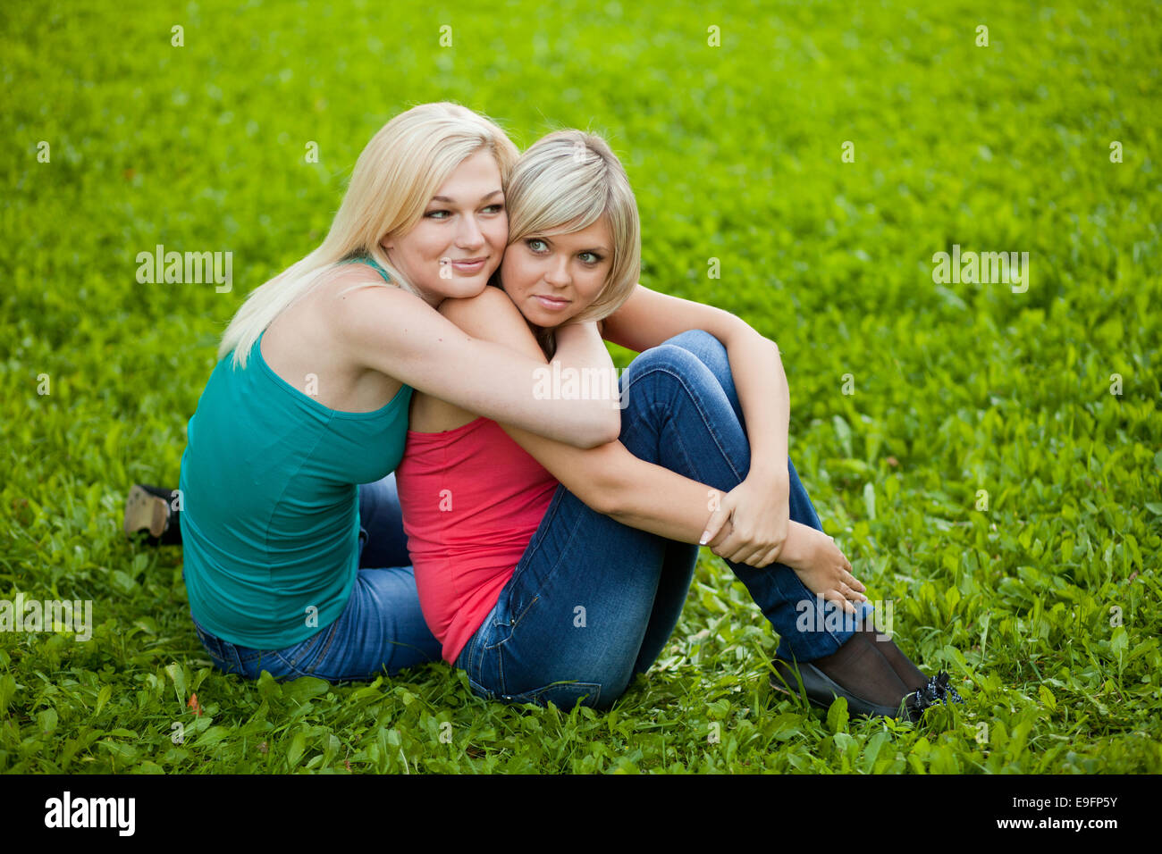 Two girls sitting on the grass, embracing Stock Photo - Alamy