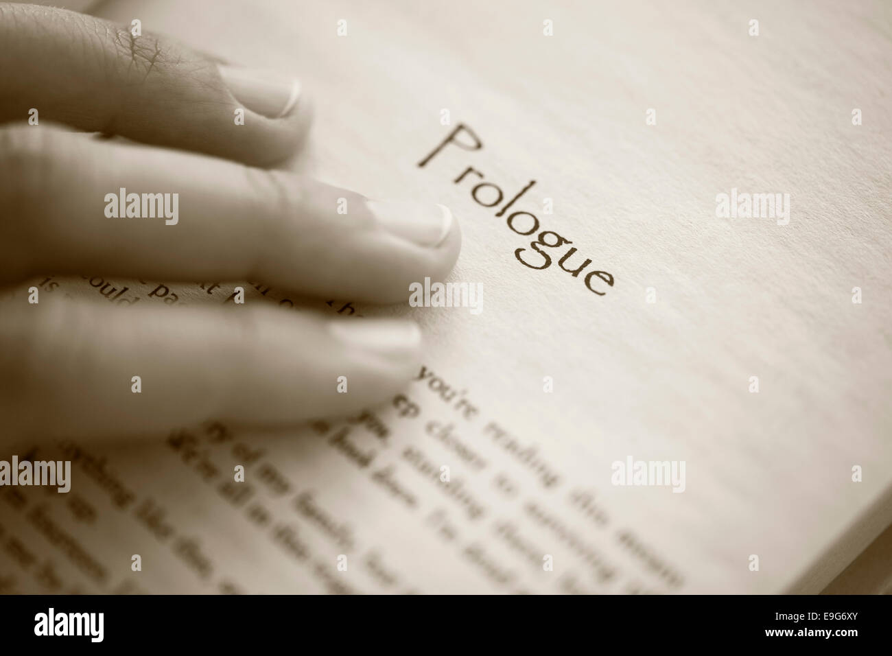 Woman's hand on book page with title 'Prologue'. Shallow depth of field. Sepia. Stock Photo