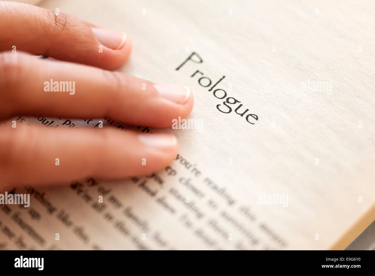 Woman's hand on book page with title 'Prologue'. Shallow depth of field. Stock Photo