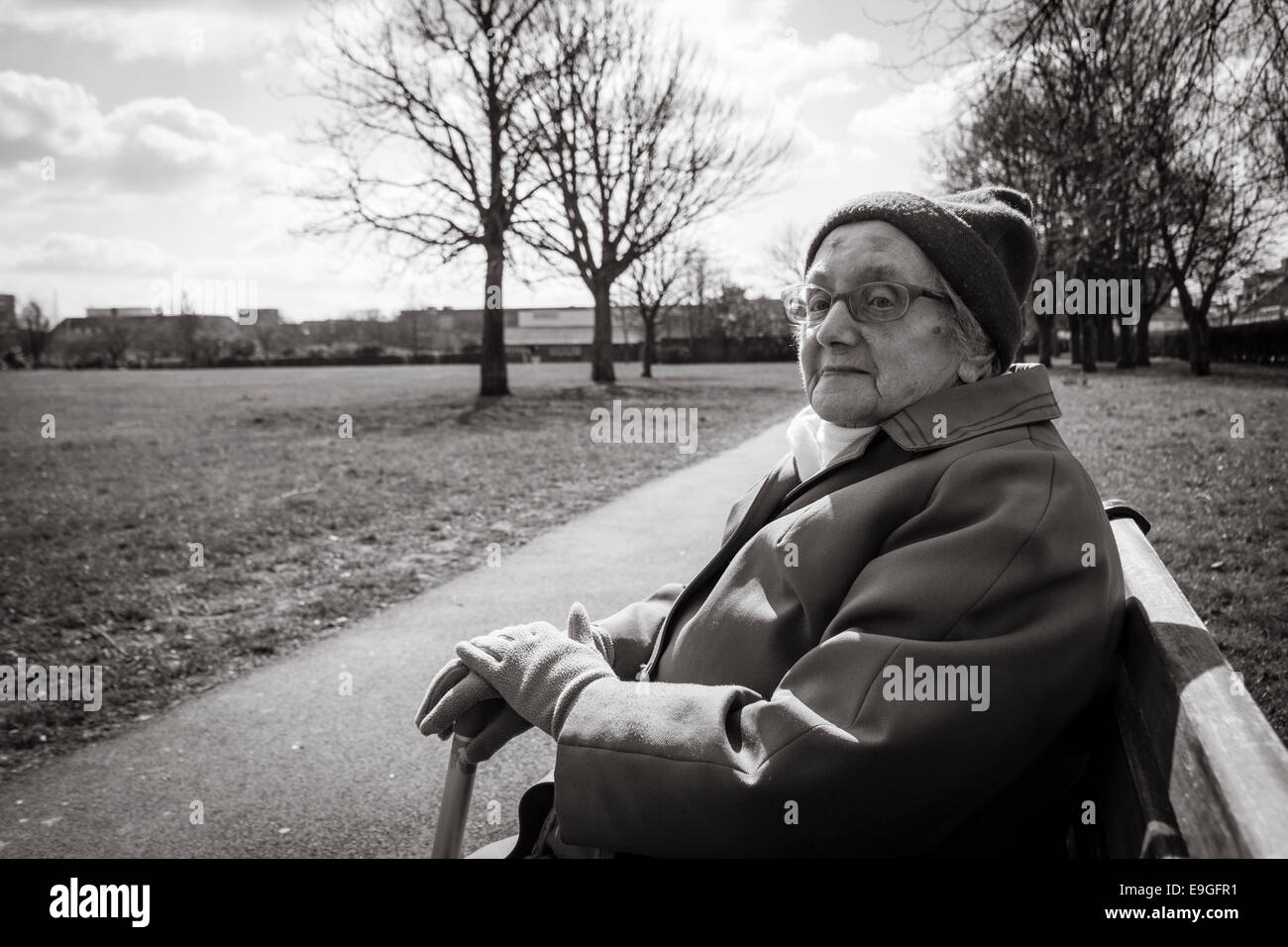 Ninety year old lady sitting on park bench in Autumn. England. UK Stock Photo