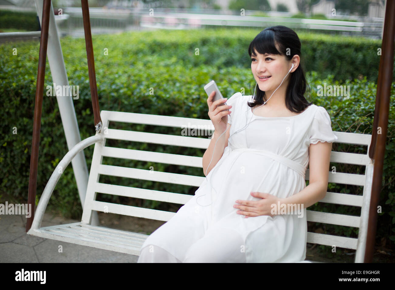 Pregnant woman listening to music on swing chair Stock Photo