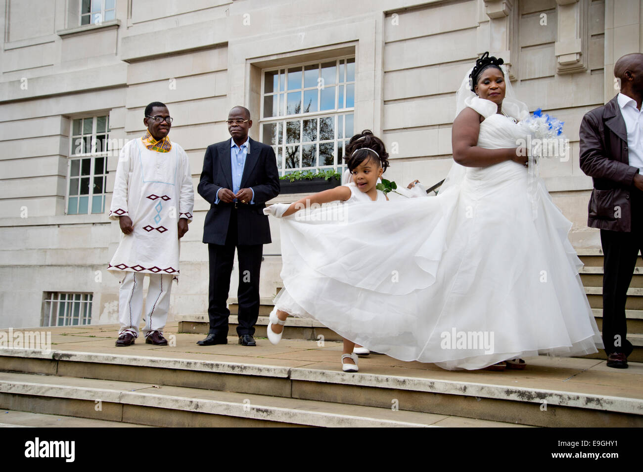 Hackney Town Hall. Registry Office wedding. Bride wearing white about to enter, with young bridesmaid holding her train. Stock Photo