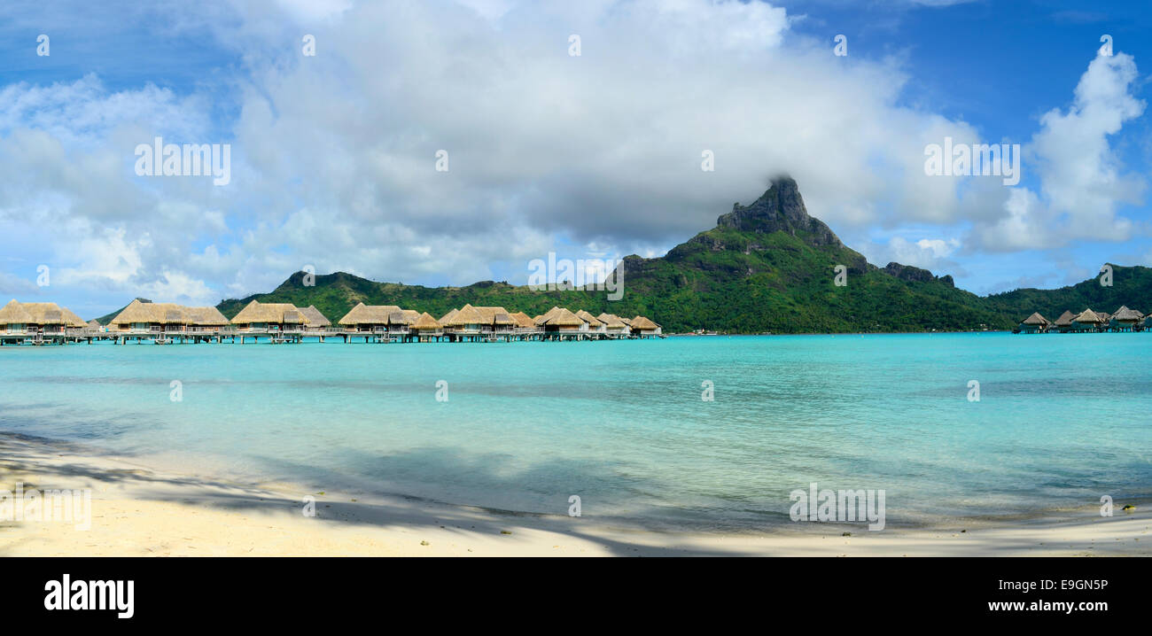 Panorama view on luxury overwater bungalows in a vacation resort in the clear blue lagoon of the tropical island of Bora Bora. Stock Photo