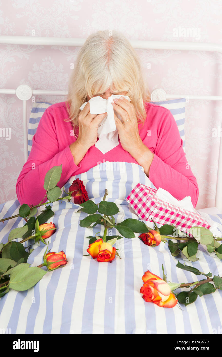 Sad woman in pink pajama sitting in bed with a bunch of roses and tissues Stock Photo
