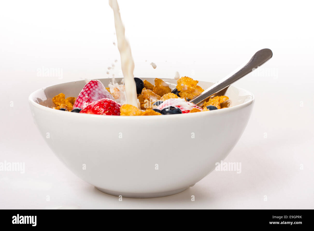 Milk poured over a fresh bowl of cornflakes with strawberries and blueberries. Stock Photo
