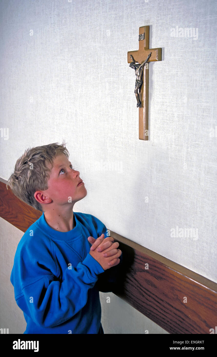 Caucasian child wearing blue shirt looking up at crucifix on wall prays with his hands folded. MR  © Myrleen Pearson Stock Photo