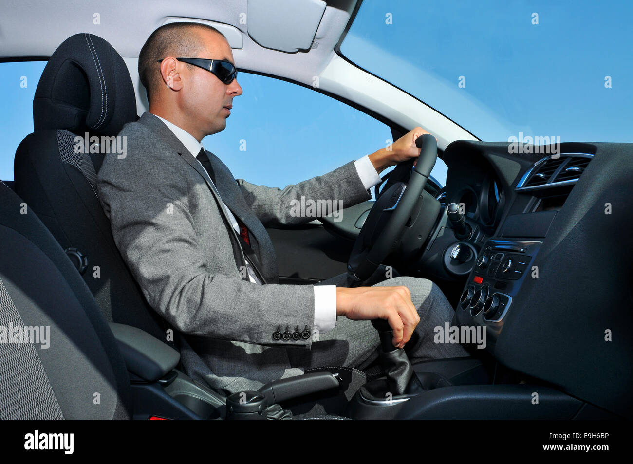 a young man wearing a suit and sunglasses driving a car with manual transmission Stock Photo