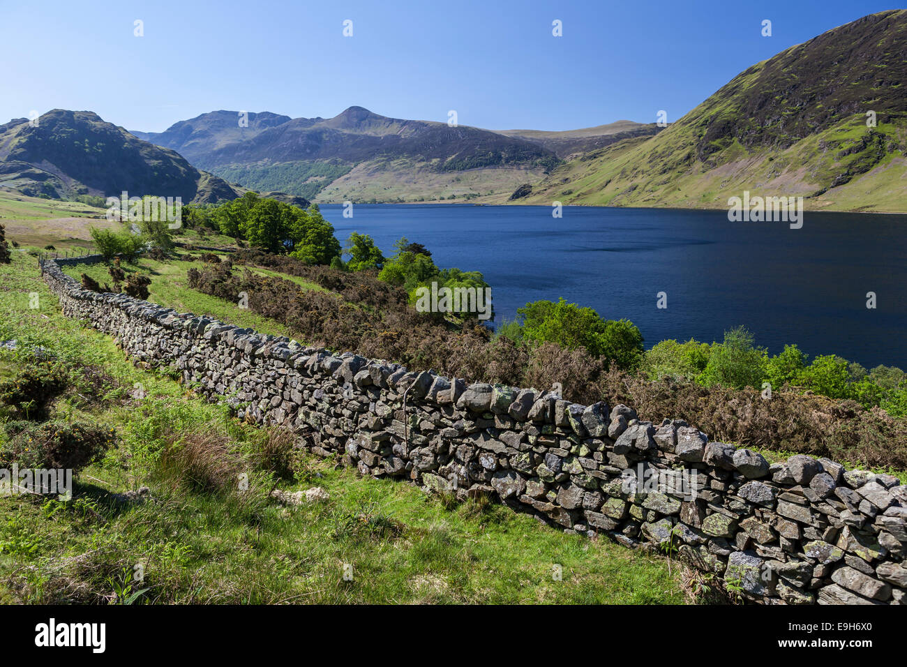 View over an old English stone wall towards the blue lake of Crummock Water, Lake District National Park, Cumbria, England Stock Photo