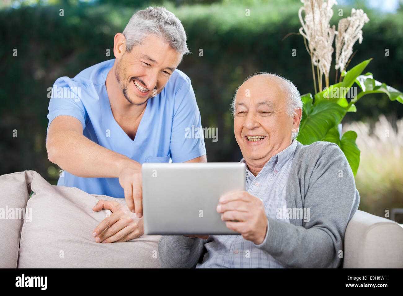 Male Nurse And Senior Man Laughing While Using Digital Tablet Stock Photo