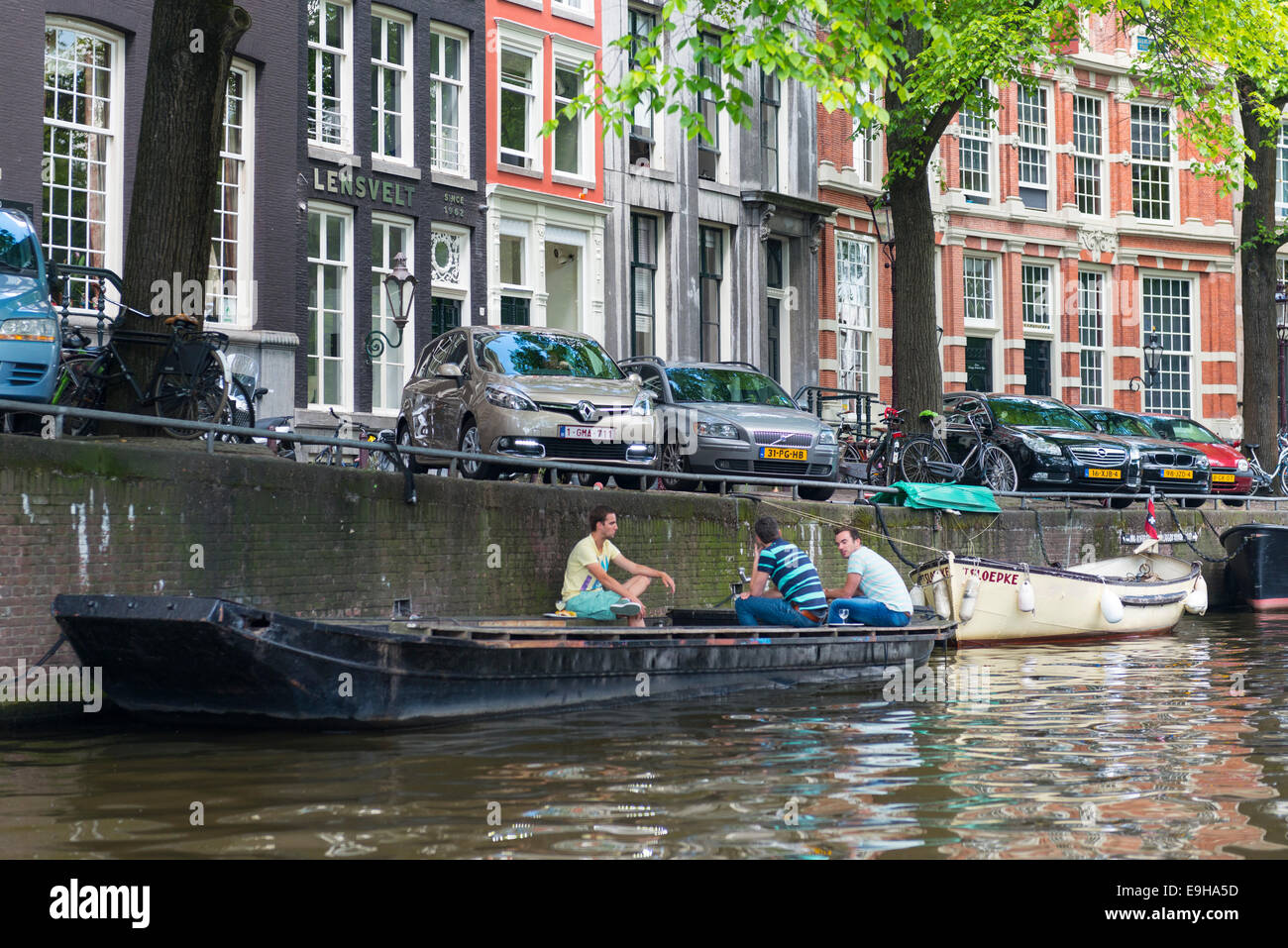 Three young men sitting on boat chatting on a canal in Amsterdam, Netherlands Stock Photo
