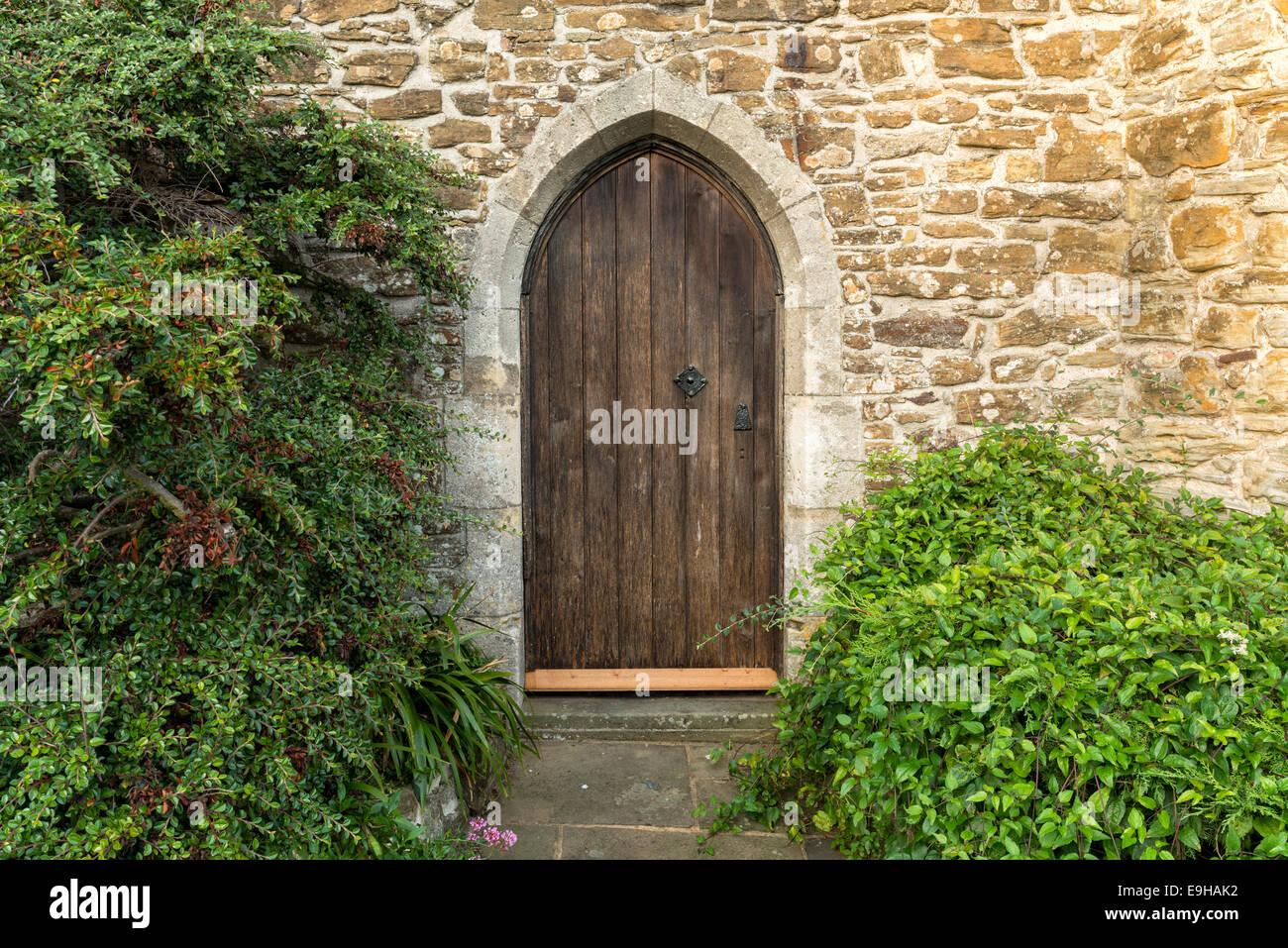 An old arched heavy wooden door set in an ancient stone wall Stock Photo
