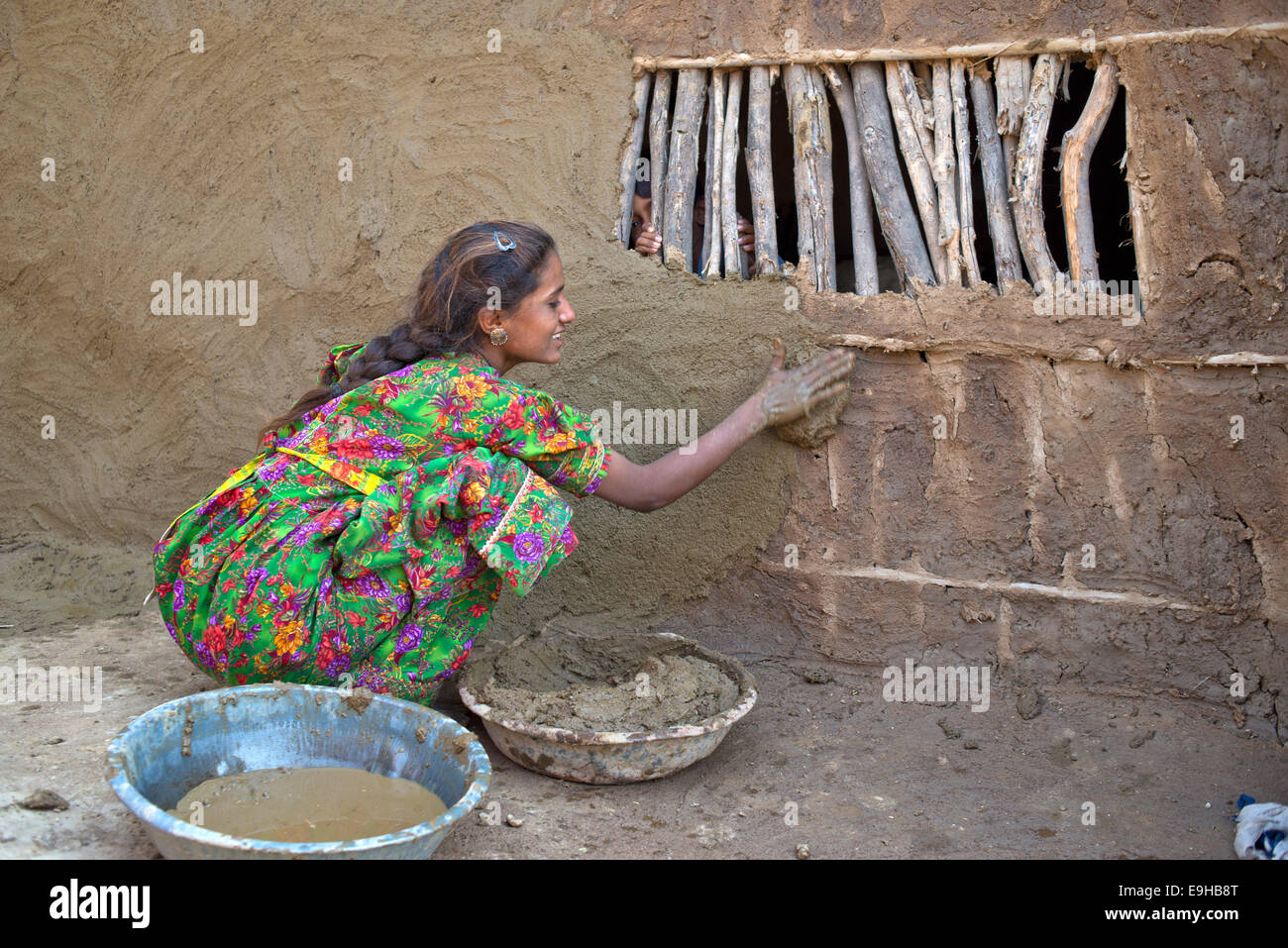 Girl in traditional dress plastering the wall of a house with a mixture of water, sand and cow dung, Rann of Kutch, Gujarat Stock Photo