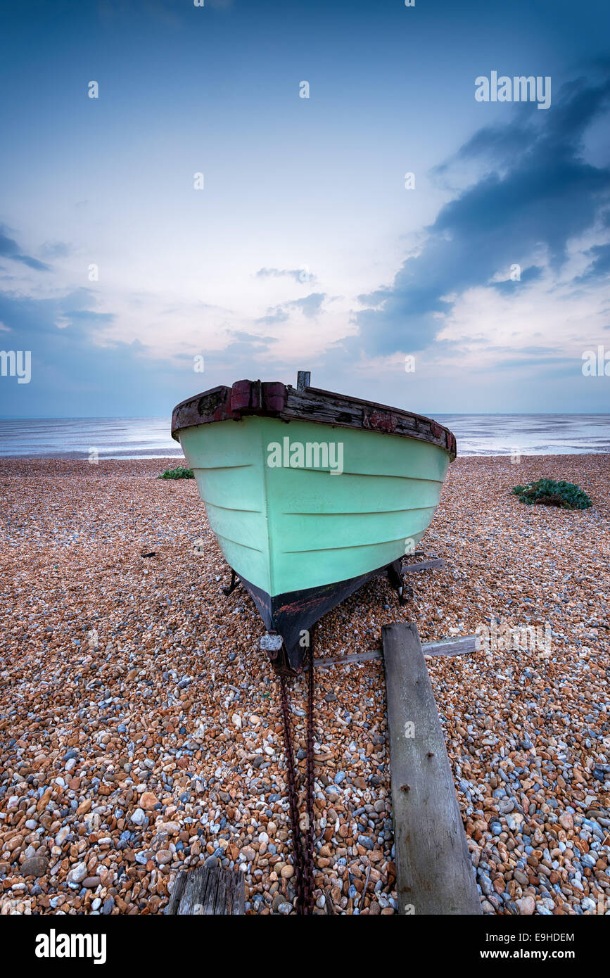A green fishing boat on a pebble beach at Lydd on Sea in Kent Stock
