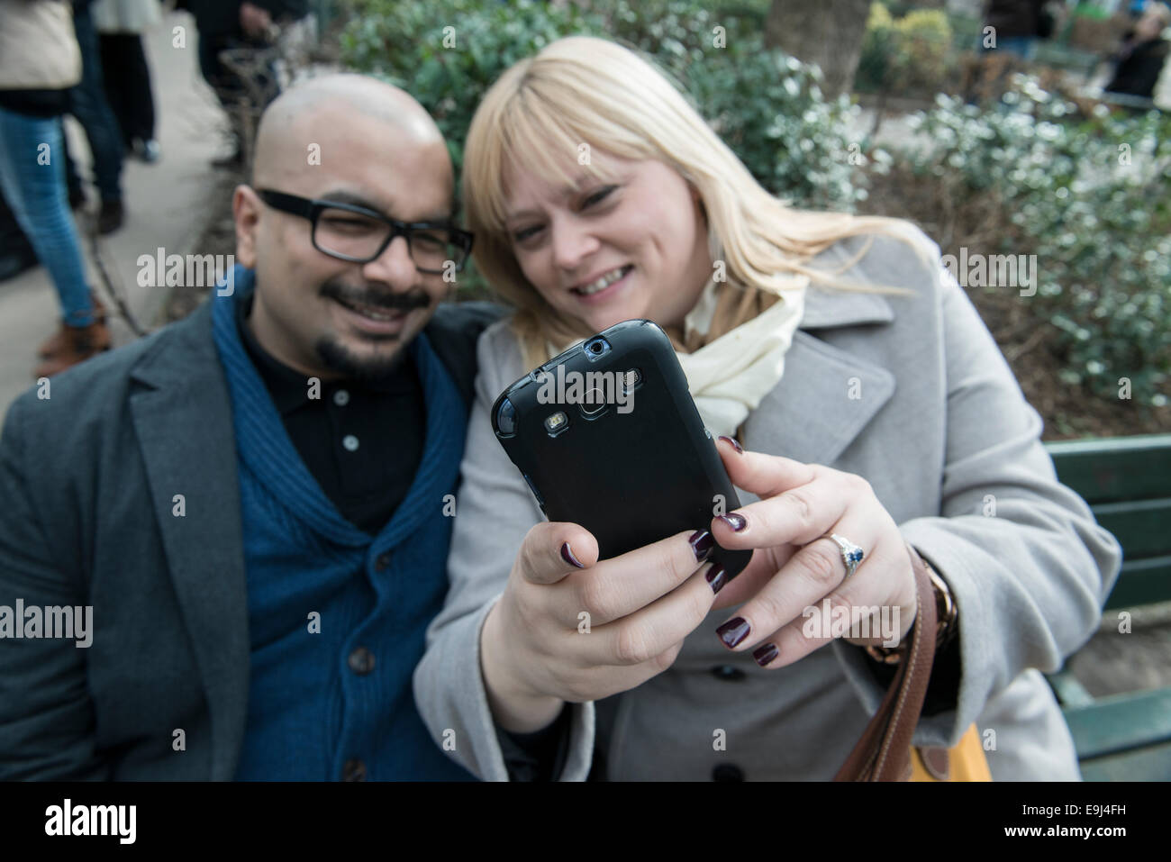 a real authentic couple sit on a bench in paris and take a selfie on a smart phone while looking happy Stock Photo