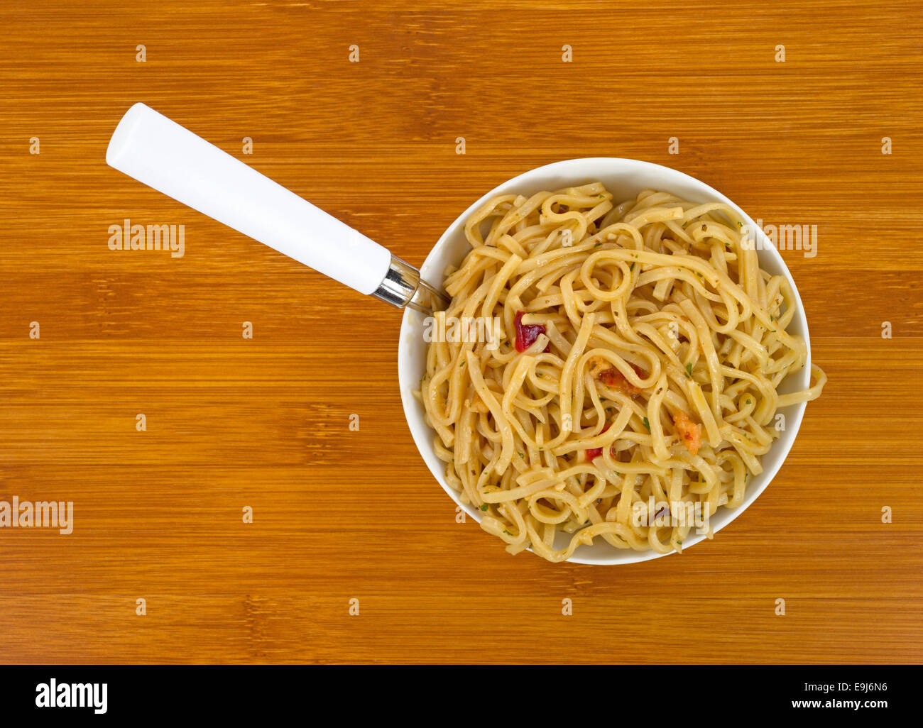 Close view of a serving of Chow Mein noodles with shrimp and seasonings in a small bowl with a fork in the meal on a wood table Stock Photo