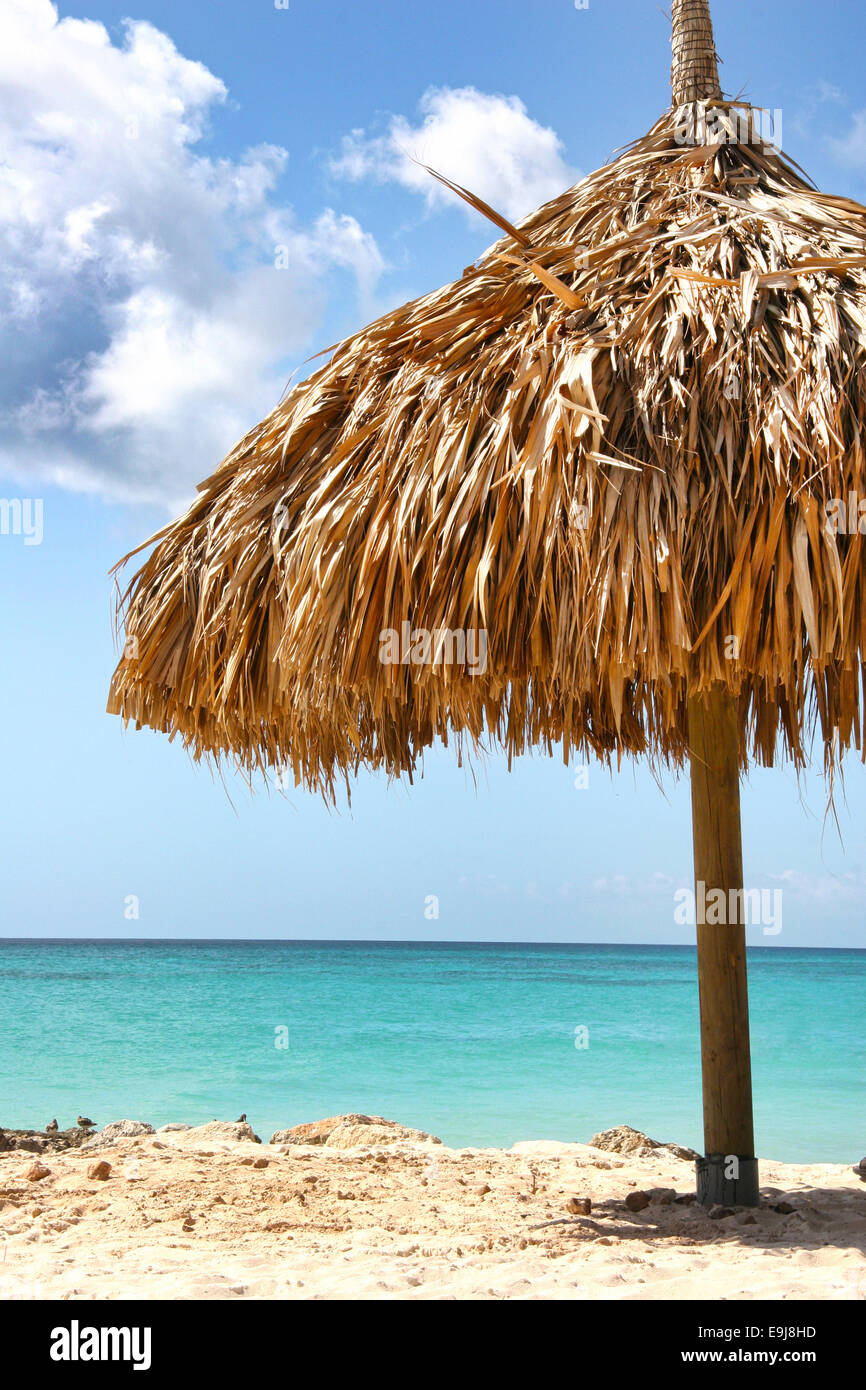 Natural straw umbrella giving shade on the beach, with turquoise sea & blue sky, Manchebo Beach, Aruba, Caribbean. Stock Photo