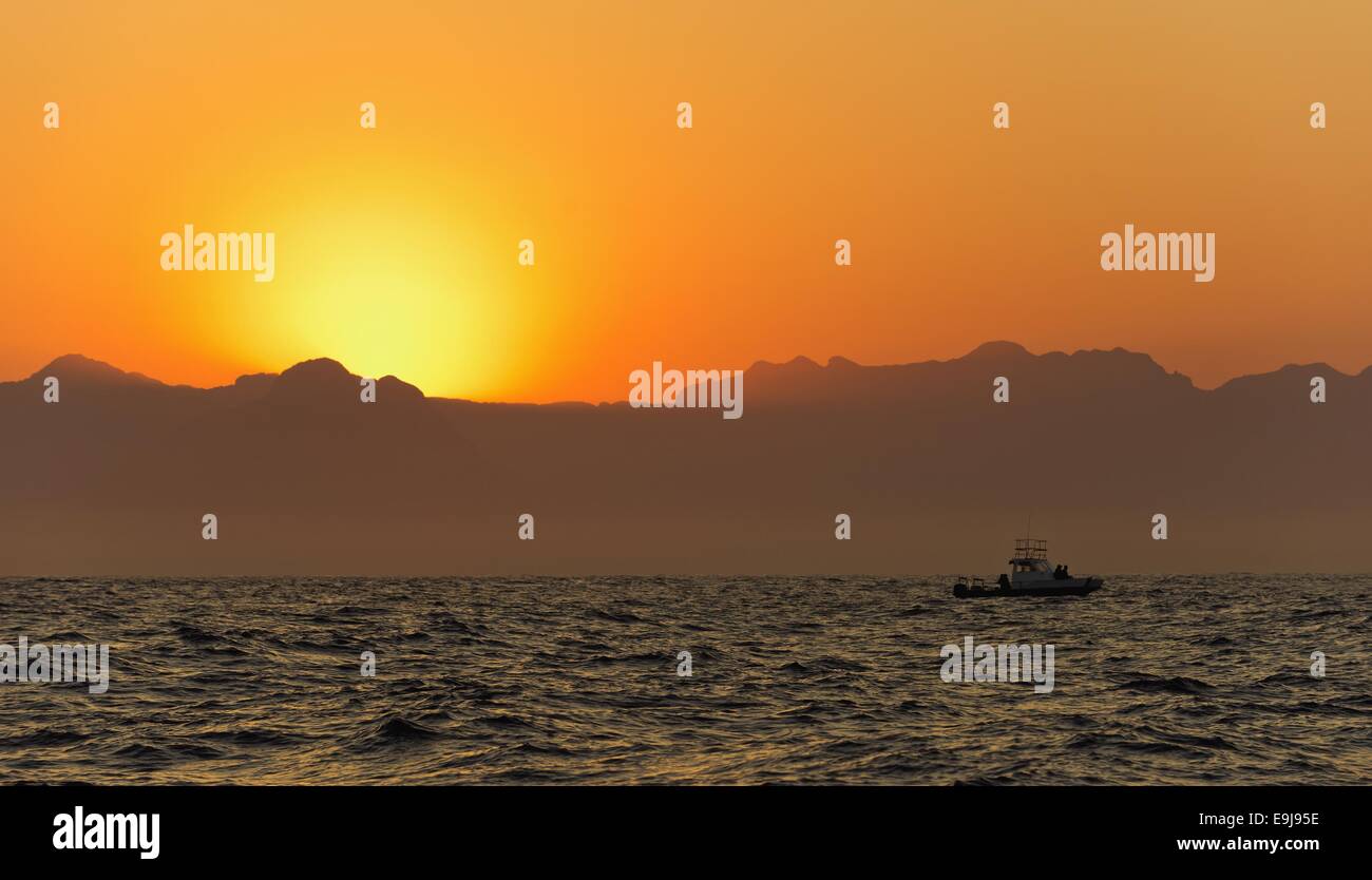 Orange sunrise at the ocean with mountains silhouettes Stock Photo