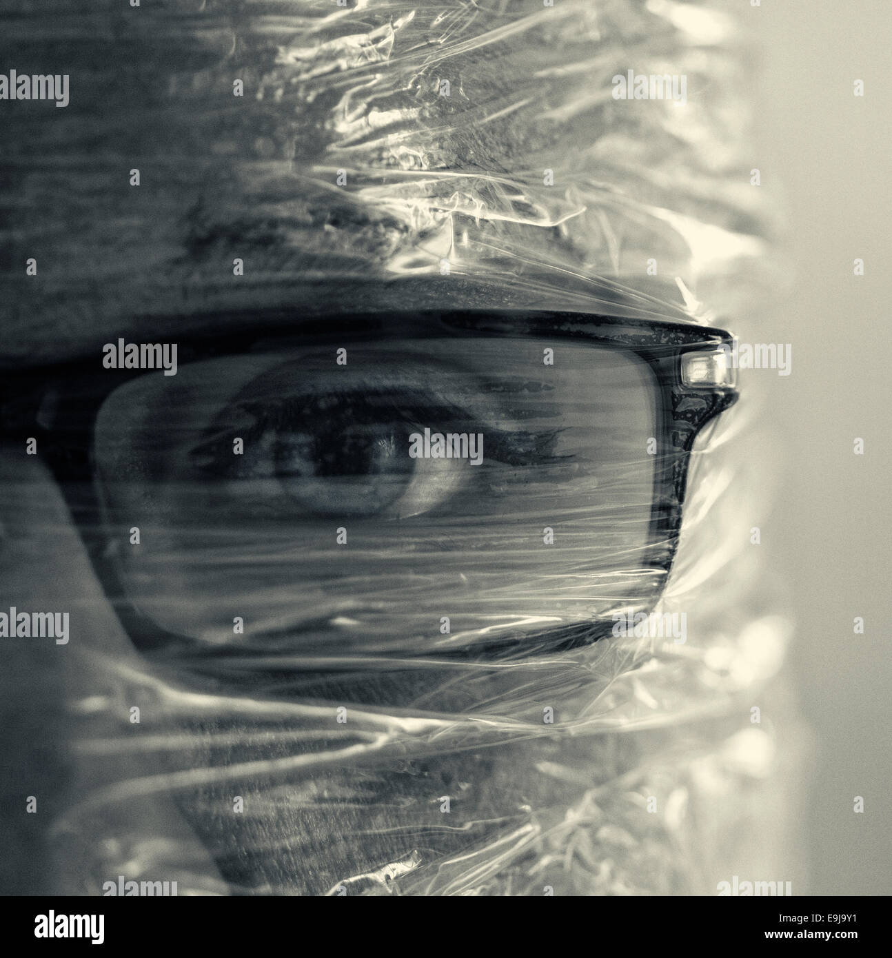 A section of a womans face, who is wearing glasses, wrapped in cling wrap. Stock Photo
