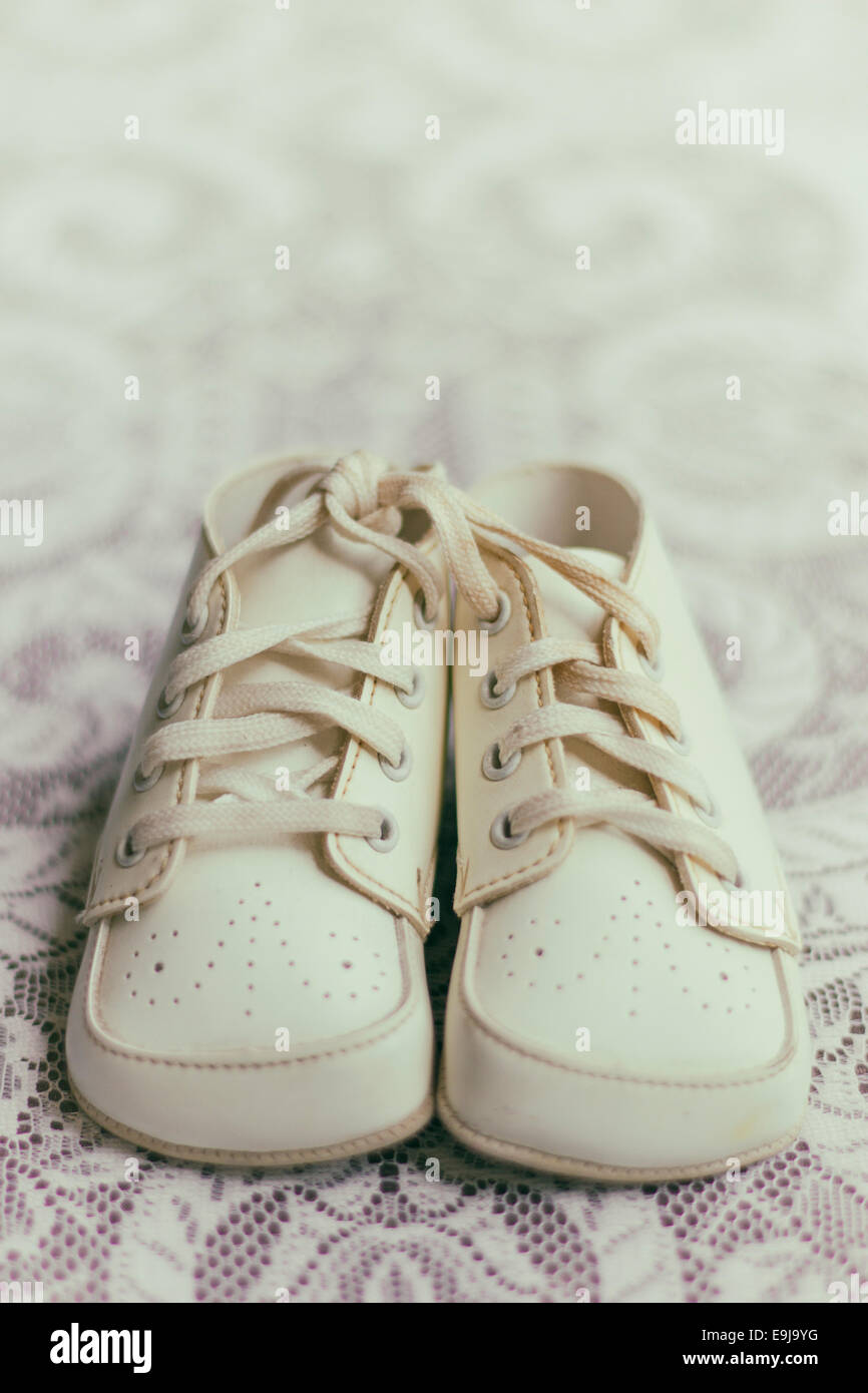 A pair of unused vintage baby shoes sit on a lace covered tabletop. Stock Photo