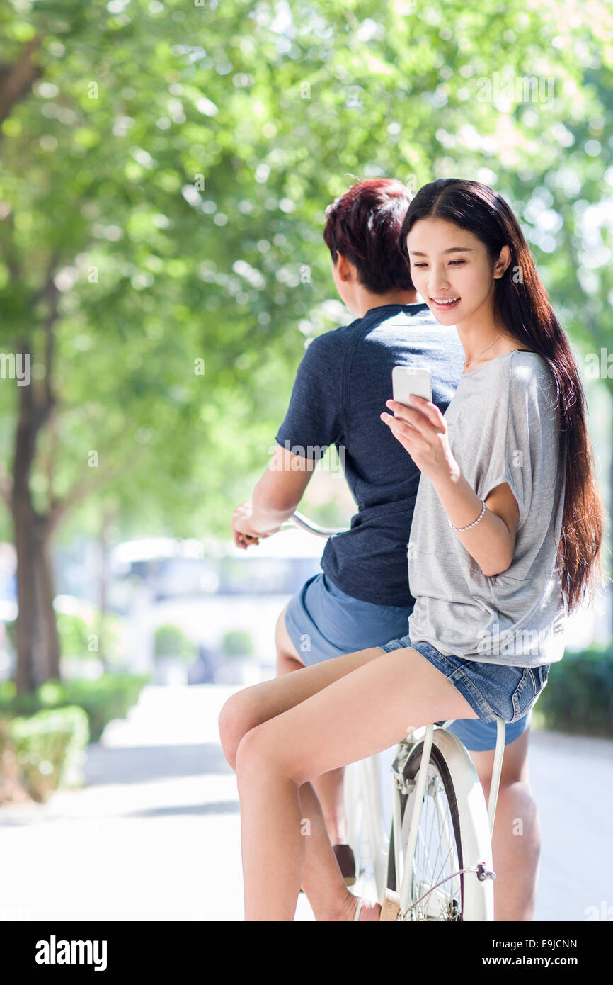 Young woman sitting on boyfriend's bicycle with smart phone Stock Photo