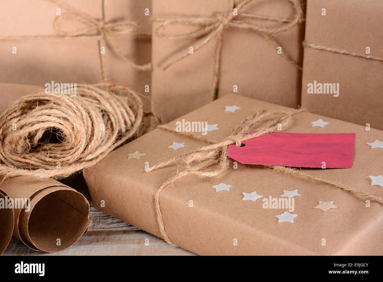 Closeup of a group of Christmas packages wrapped with plain brown paper and twine. Horizontal format on a wood table. A red gift Stock Photo
