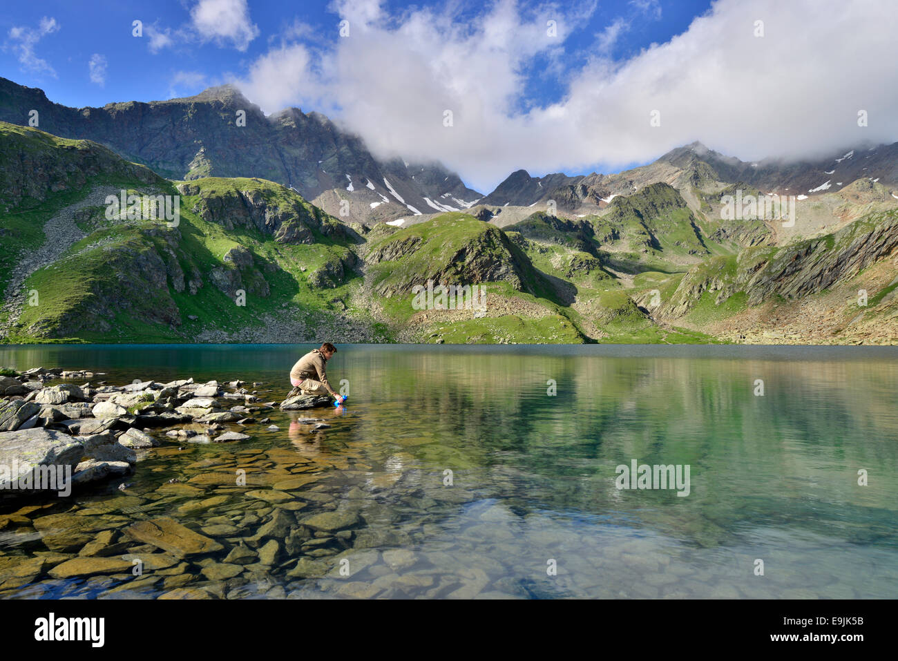 Mountaineer filling a water bottle at Grosser Schwarzsee Lake or Lago Nero, Mount Schwarzwandspitze at back, Stubai Alps Stock Photo