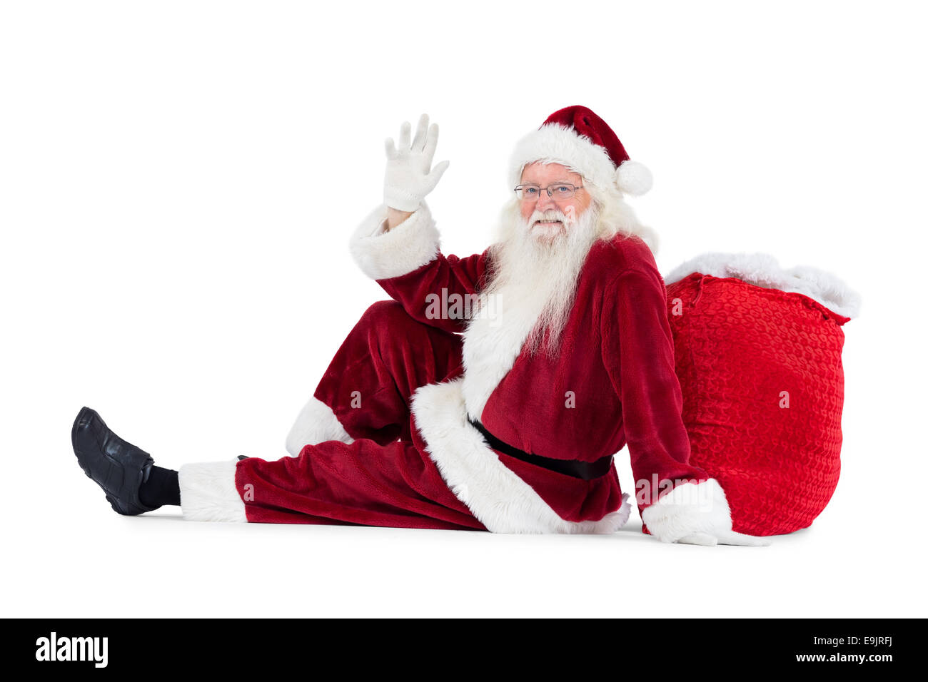 Santa sits leaned on his bag and waves Stock Photo