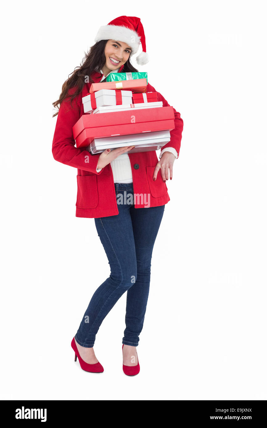 Festive brunette in santa hat and red coat holding pile of gifts Stock Photo